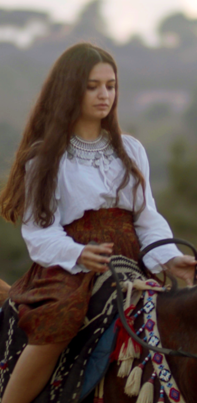 A girl adorned with traditional clothes and jewelry on the back of a horse. 